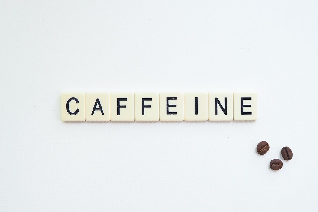 letters of the word caffeine written in block and three coffee beans are shown