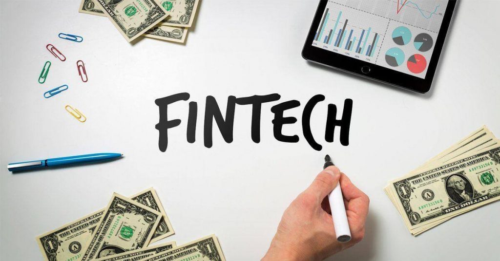 Picture is showing money and a hand is writing fintech on a board. 
